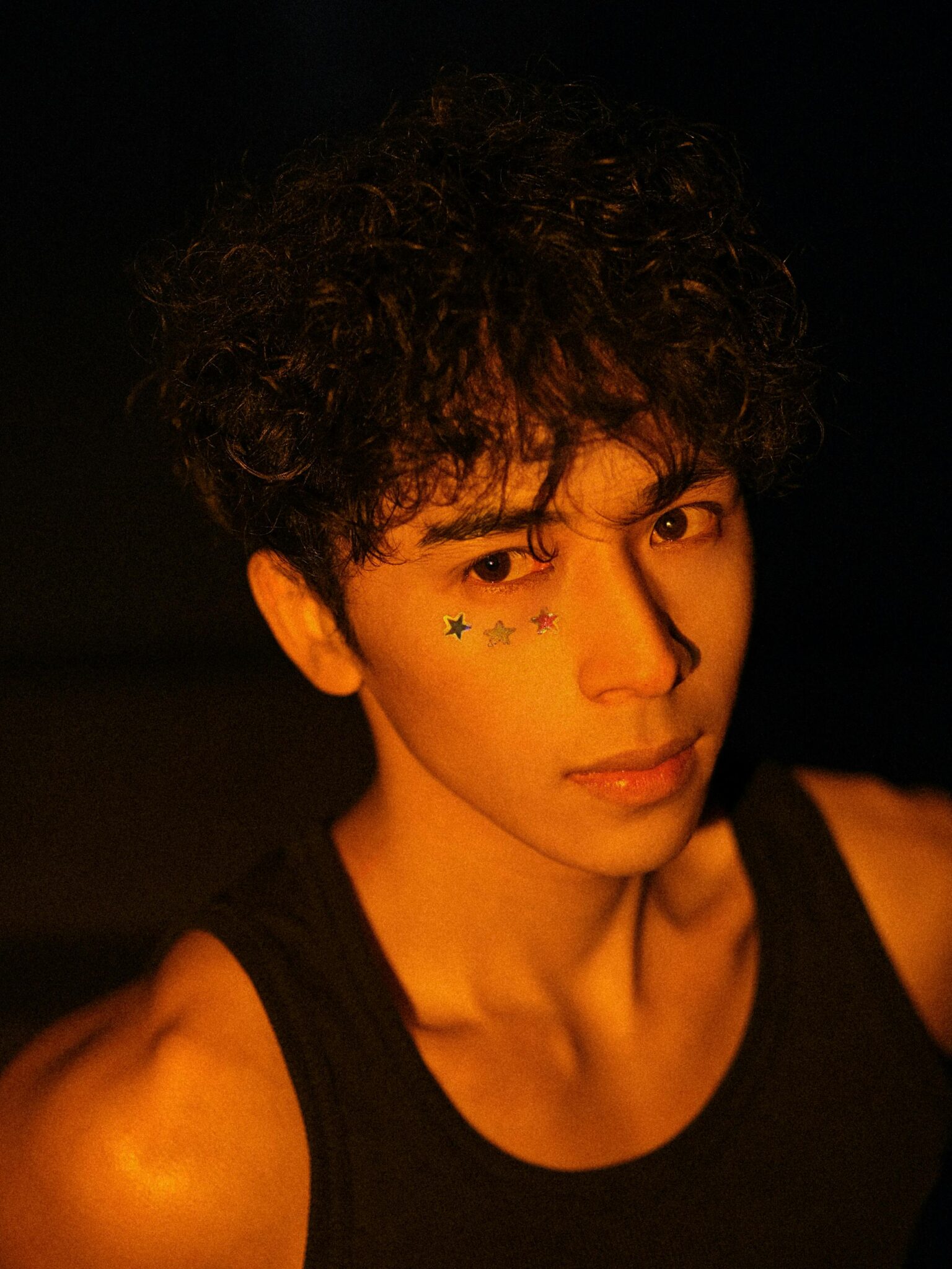 Close-up portrait of young man wearing star stickers on his face, in warm light.