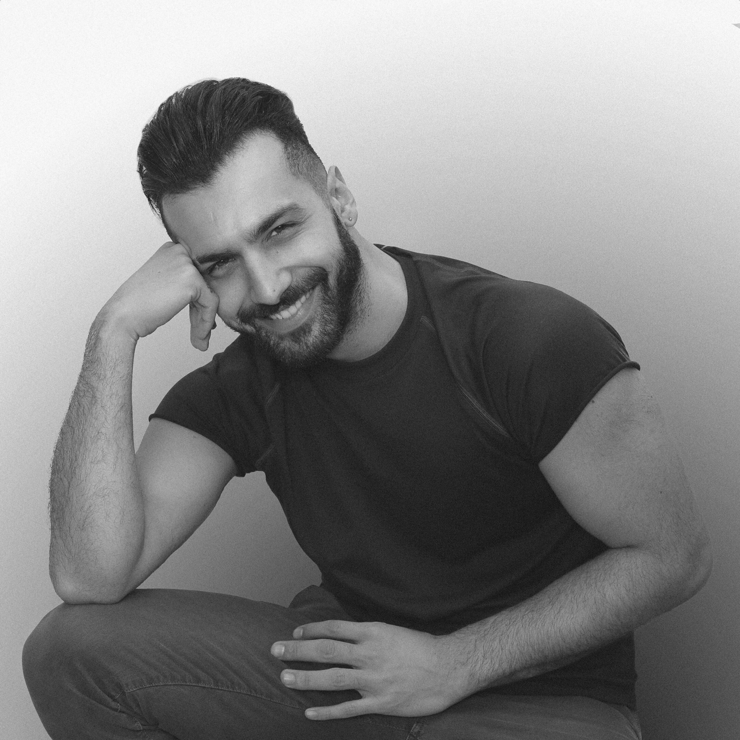 Portrait of a smiling man with facial hair, sitting indoors in a studio setting.